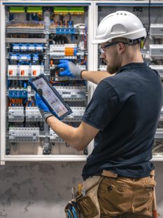 Electrical technician working in a switchboard with fuses, uses a tablet. Electrical technician looking focused while working in a switchboard with fuses. SSUCv3H4sIAAAAAAAACpySwW6DMAyG75P2DijnIgGBju5Vqh1MSMFqmlRJ6DRVffc5CaDsOnHBn+3f/jHP97eiYAM4FOyzeIaIYlRqcd6CR6MJV4eVW6lHaXPysPxY5QAwj+SI3lgElcMBvJg13CRBvSgV8CsmmfPgFydd2GVFArycSCPBXSItfE5xsSVikjooxdghY24ZIttQEv9XZ3r52g1PUoufuHBmxEolIRk5p1J2/fbS3nJrsIxoMlcPI0CFAp4pAd7Bwp++u0WBesqI8XO8y6YkzKK9DVvtZpgy5g6DCl/9QmPkxmdwjsrHjWezBf0F5pbN0cZHT6sqG+k4Iaw5747NBz193fZN1ZzWgnTQGUknrrMJUSyuOOauMGxAJzi1XVdBCU3Ly7aq67Lvu65seNe3cOLHgV/oFq9fAAAA//8DAIlQOhS5AgAA