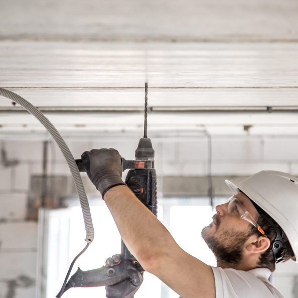Handyman uses jackhammer, for installation, professional worker on the construction site. The concept of electrician and handyman. House and house reconstruction.